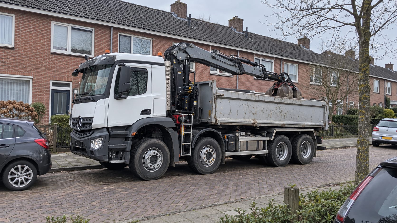 Een knijperwagen 8×4 langs de stoep in een woonstraat, de kraan ingeklapt